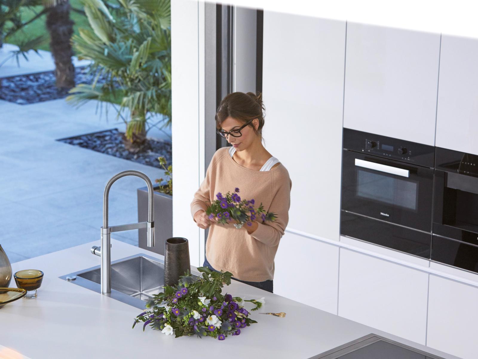 Frau arrangiert Blumen an Blanco Spüle in moderner weißer Küche