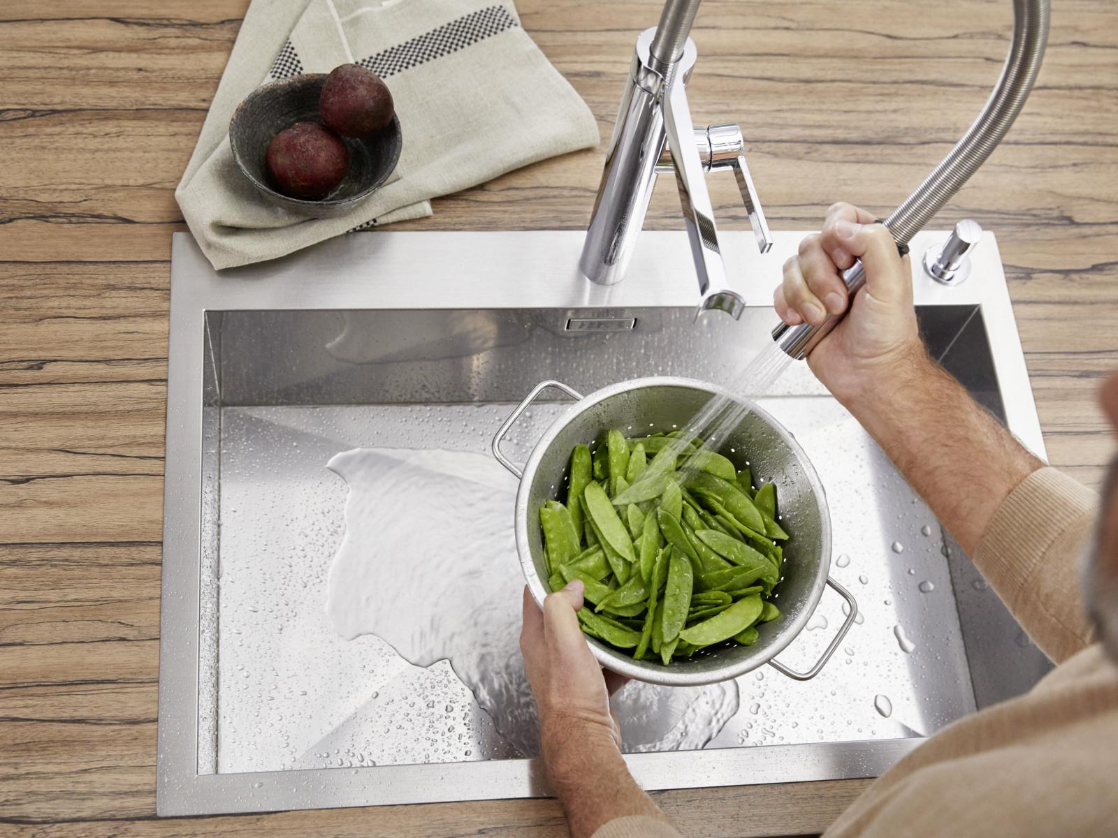 Mann wäscht Zuckerschoten in Blanco Edelstahlspüle